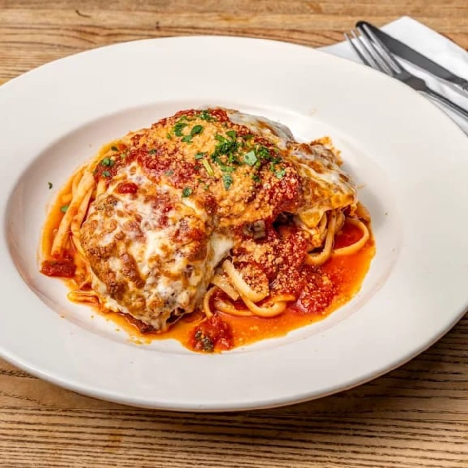 Il Forno a Legna's Chicken Parmigiana with linguine, marinara sauce, and melted cheese on a white plate.