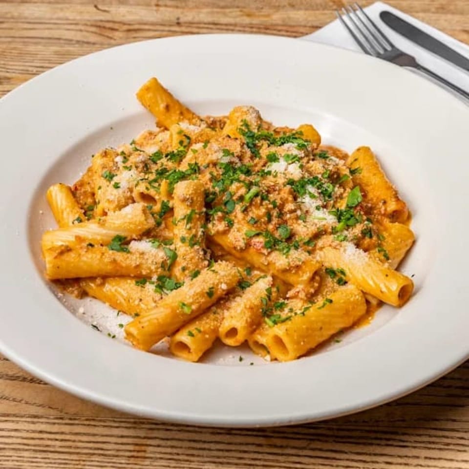 Rigatoni pasta in a creamy orange sauce, topped with grated cheese and fresh parsley on a white plate.